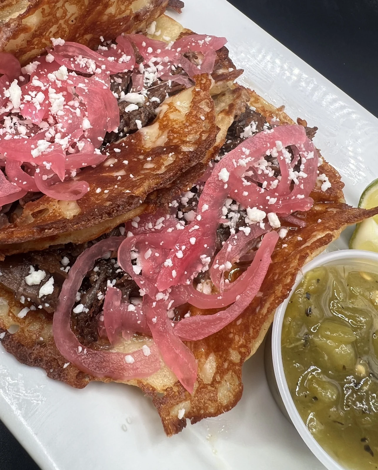 Crispy tacos with pickled onions, crumbled cheese, and green dipping sauce