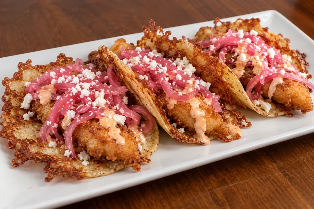 Crispy fish tacos with cheese crusts, pickled onions, cotija, and bang bang sauce